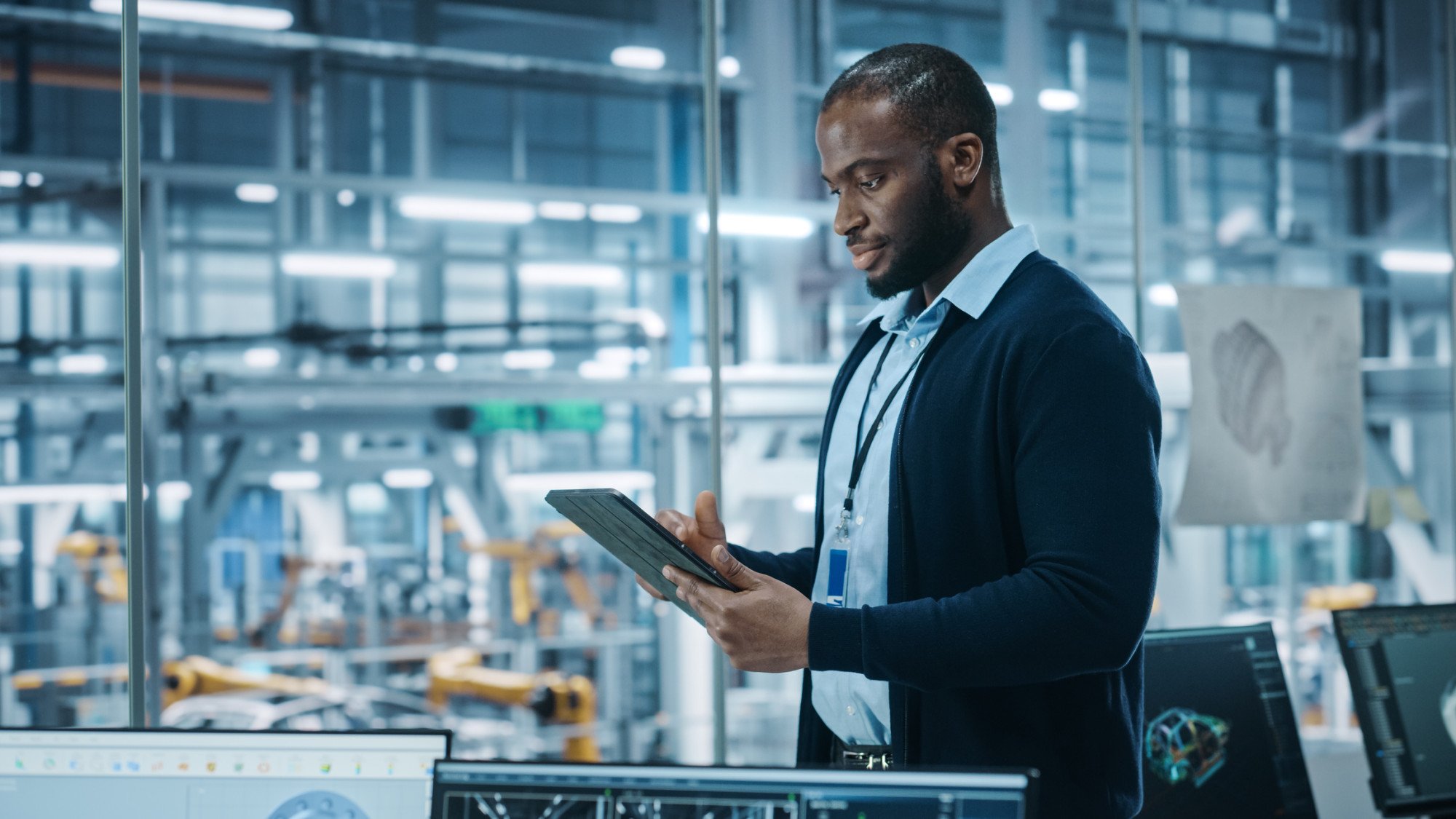 Business professional using a tablet in a modern automated manufacturing facility, showcasing the integration of AI in industrial operations.