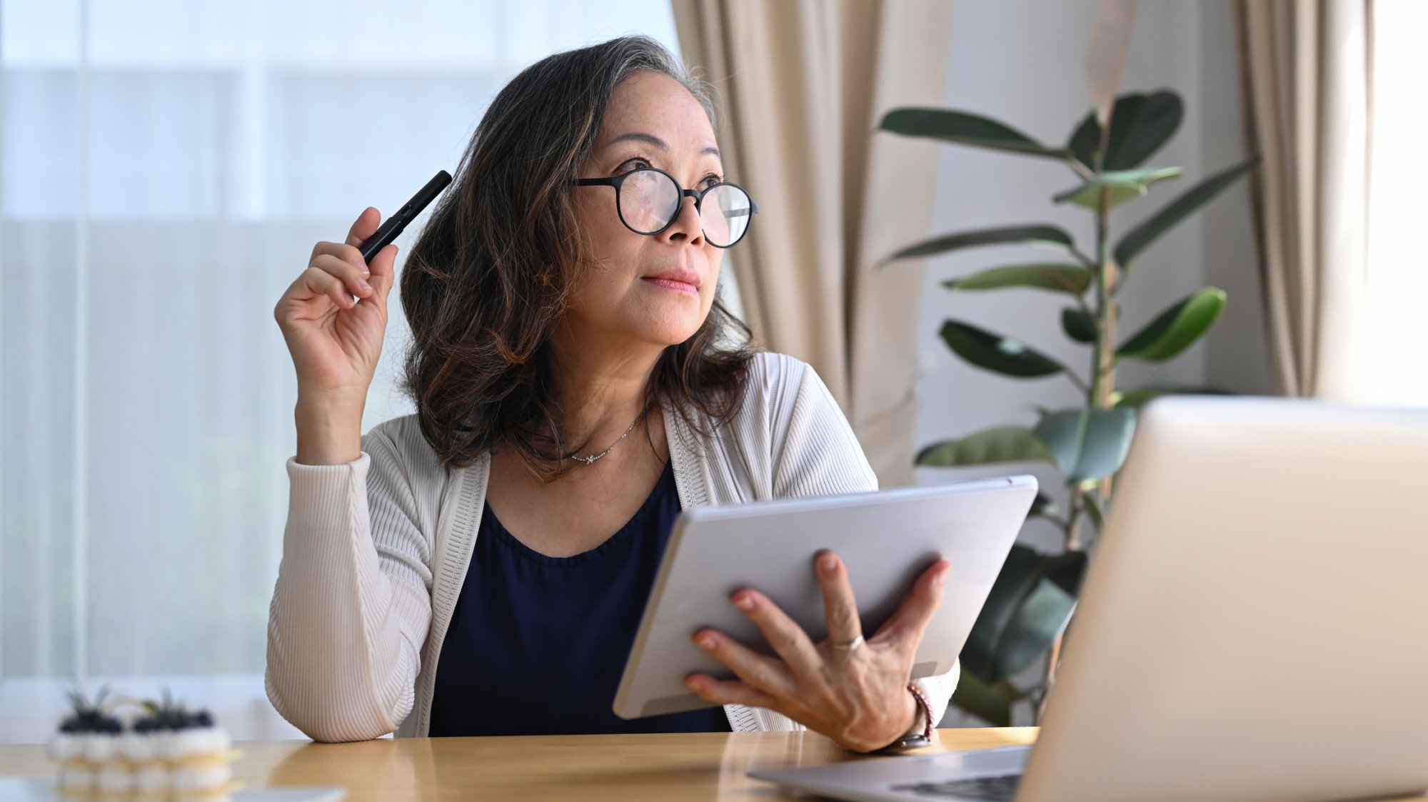 Thoughtful senior professional working with a tablet and laptop, considering cloud accounting solutions.