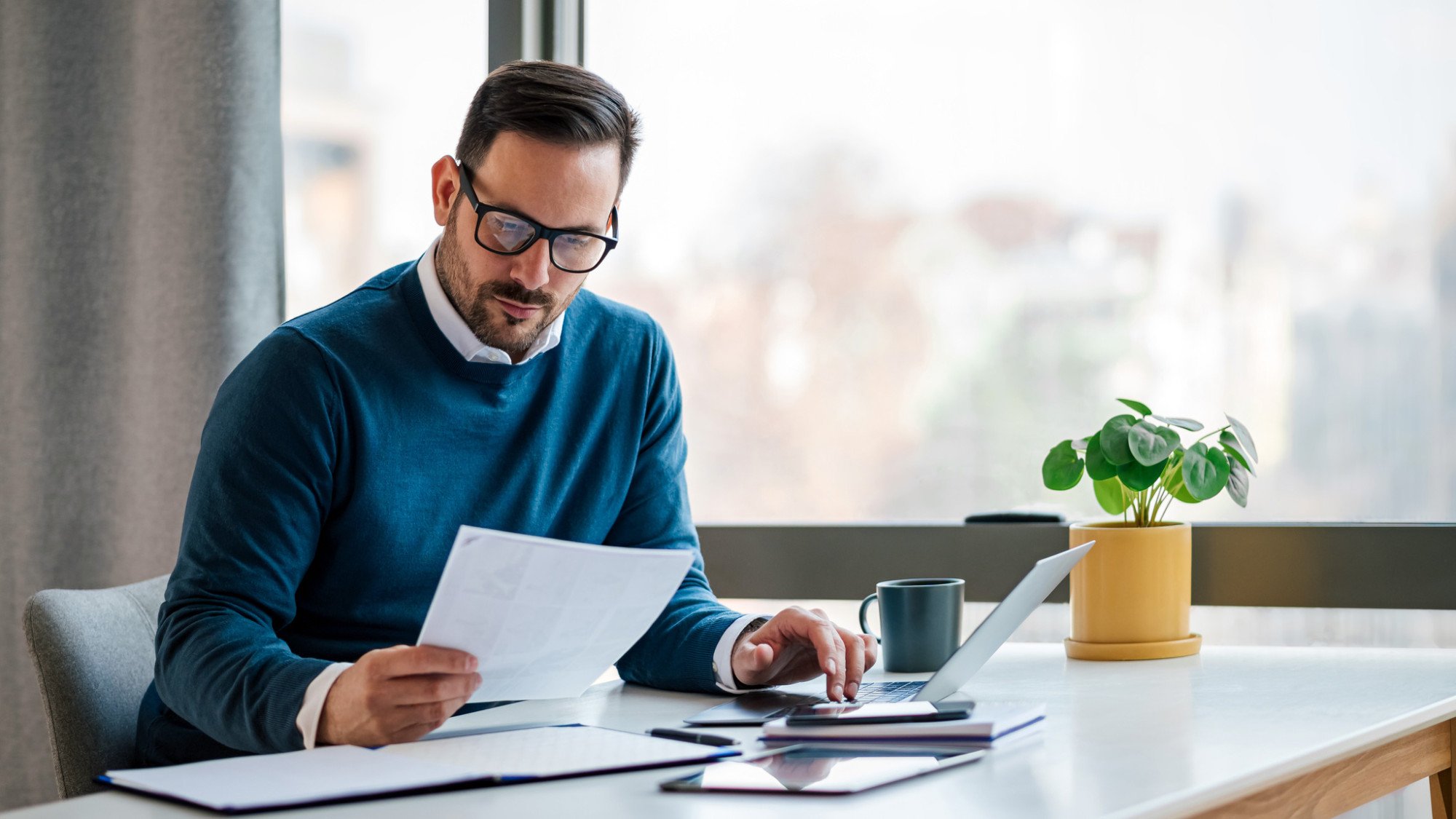 A young businessman sits at a desk looking over company documents and tax files.