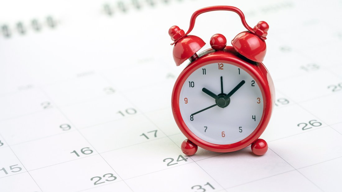 A red alarm clock sits on a desk calendar.