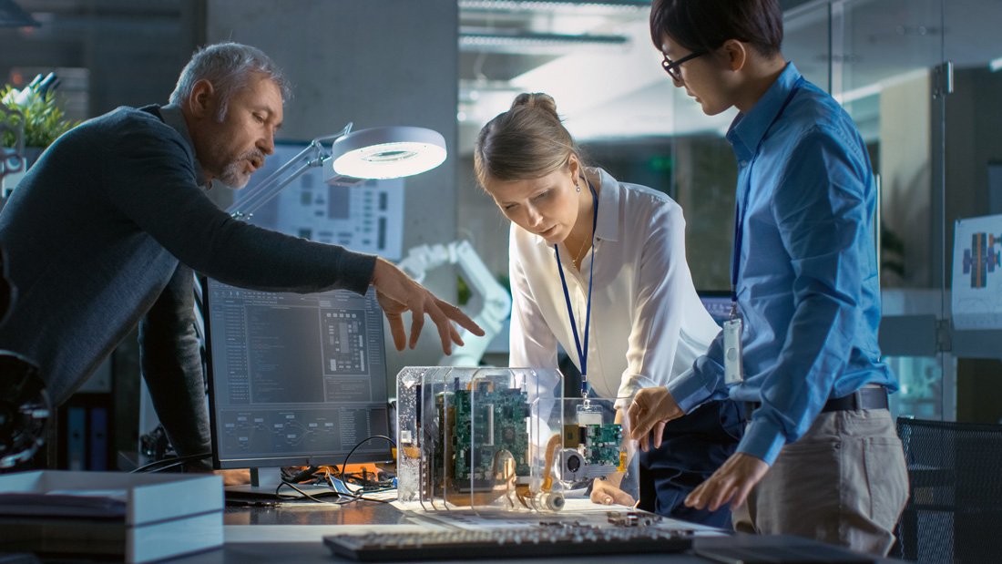 Three engineers collaborate on a technology research project, examining a transparent prototype device in a modern lab setting.